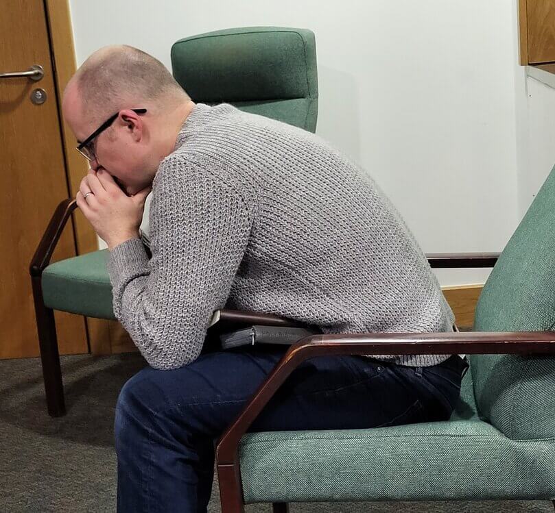 Person leaning forward on their chair, head rest on hands in praying position